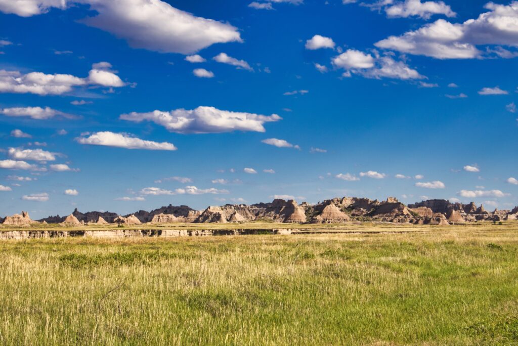Beautiful landscape of Badlands National Park under a clear blue sky with scattered clouds.