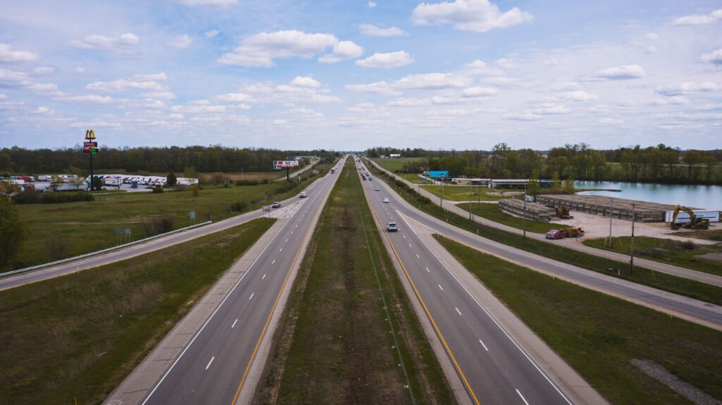 Drone view of modern vehicles riding along asphalt roadway near river against blue sky with white clouds on summer day