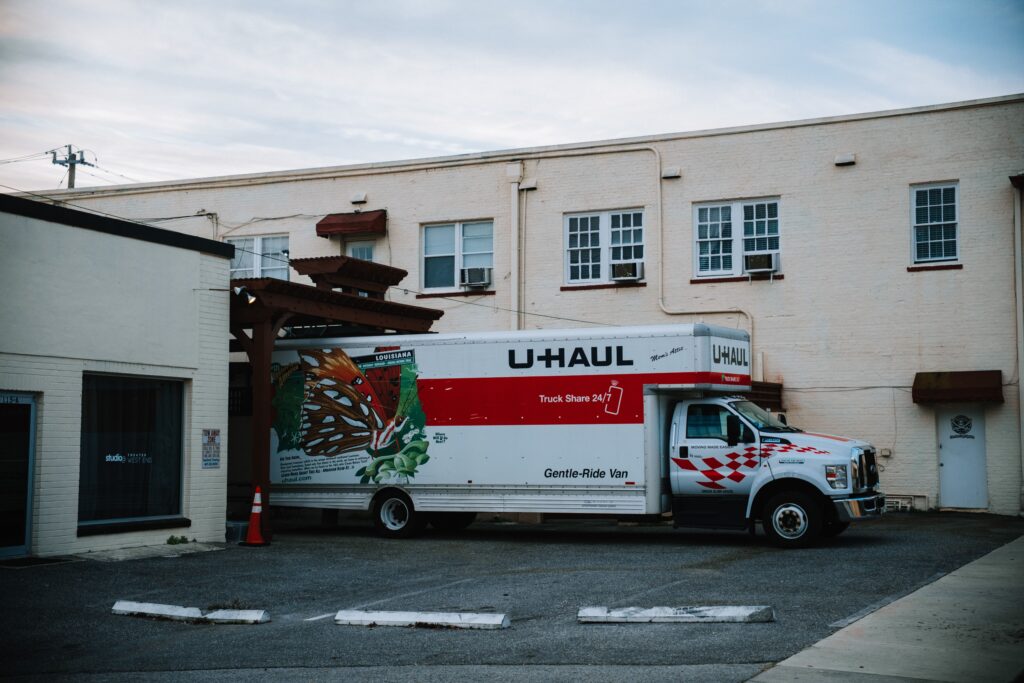 A U-Haul moving truck parked in front of a beige warehouse building.