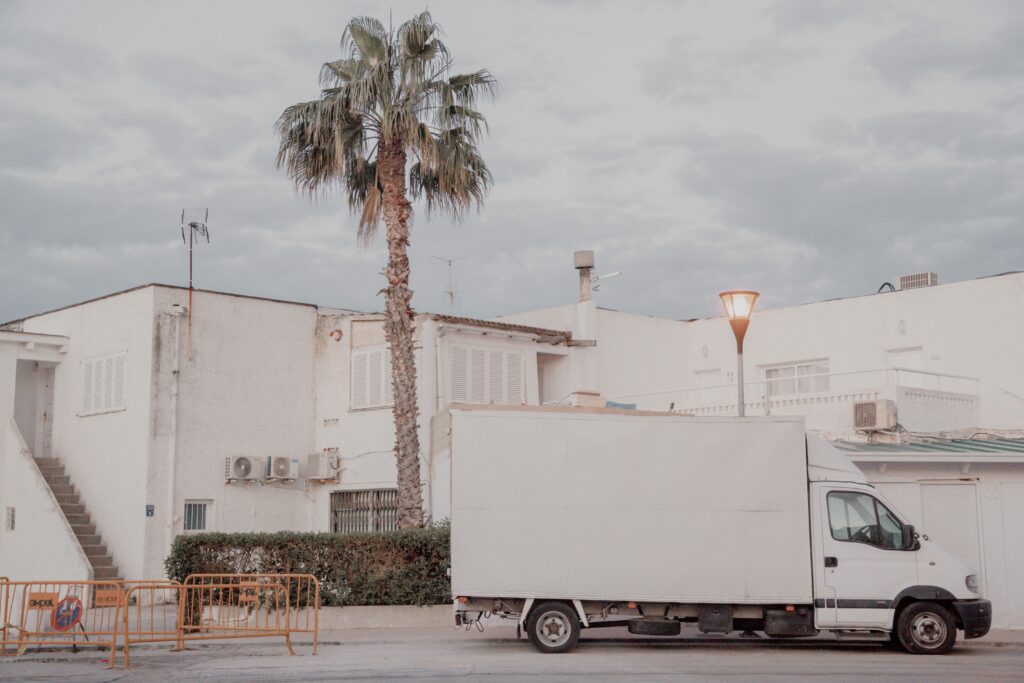 White delivery truck parked next to a white building with a palm tree in an urban setting.