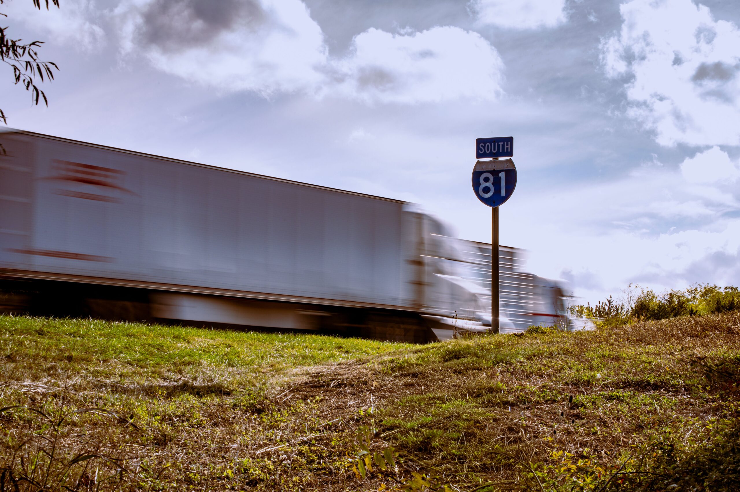 Blurred truck on Interstate 81 South with clear blue sky and grassy foreground.