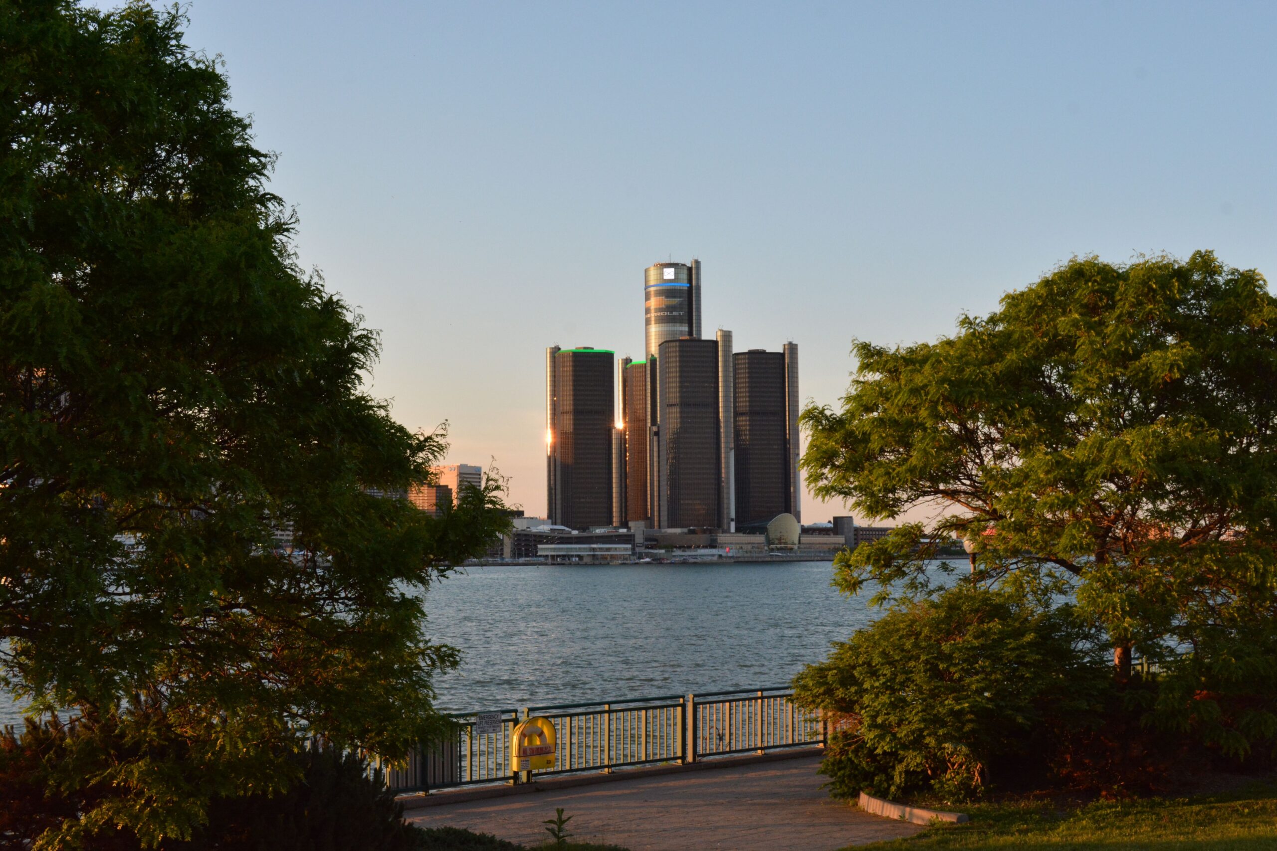 Scenic view of the Detroit Renaissance Center with lush trees framing the skyline at sunset.