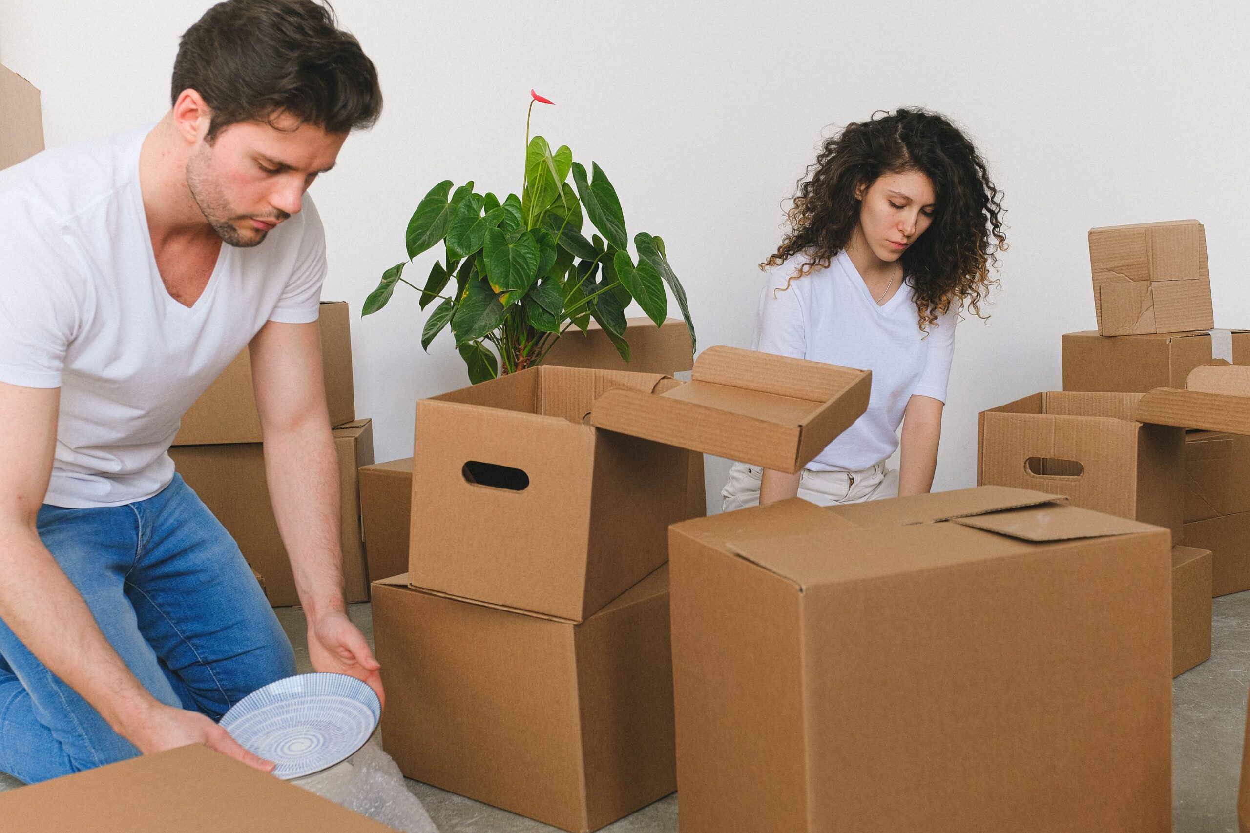 Serious young relocating man and woman in casual outfits packing fragile things into carton boxes while preparing for moving into new apartment in daylight