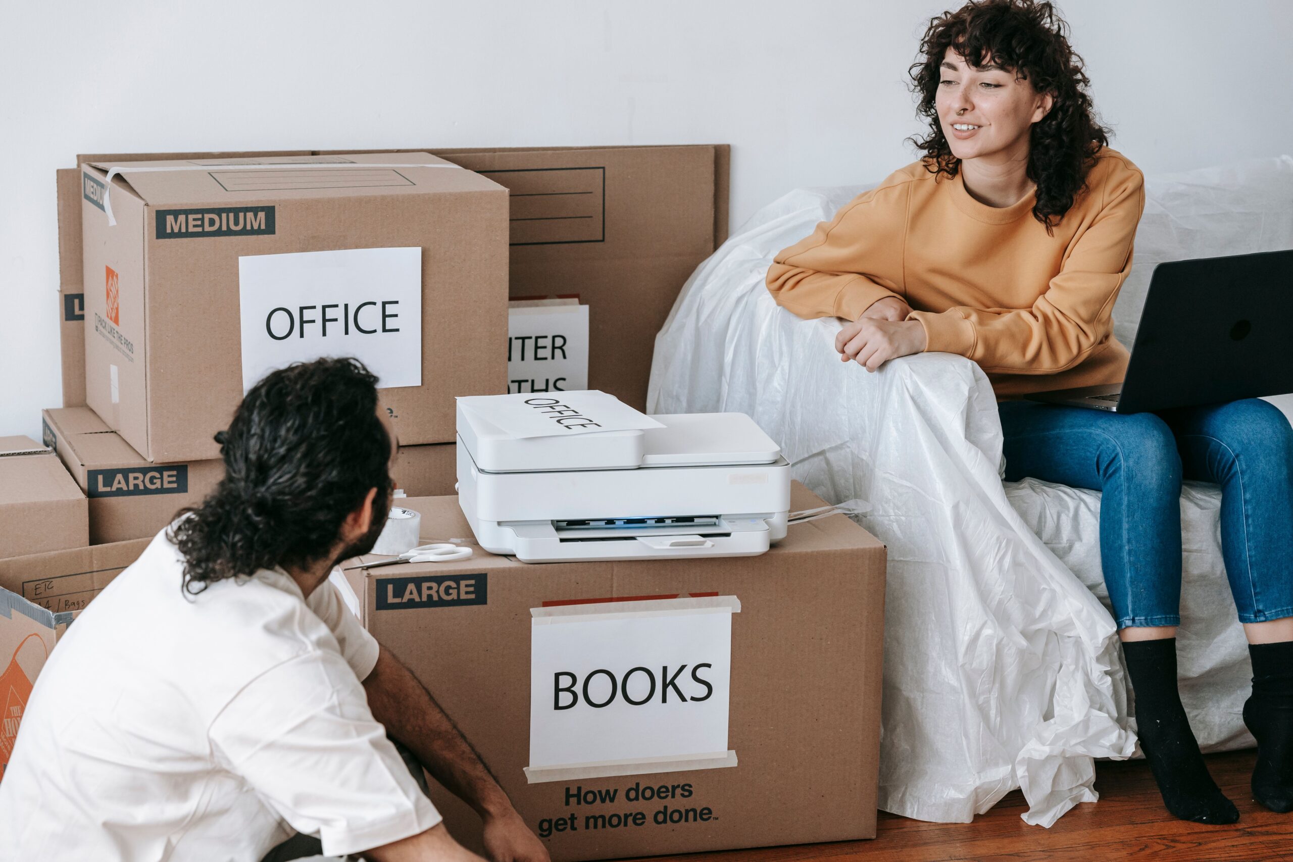 Young couple planning a home relocation with packed boxes labeled for organization and a laptop for coordination.