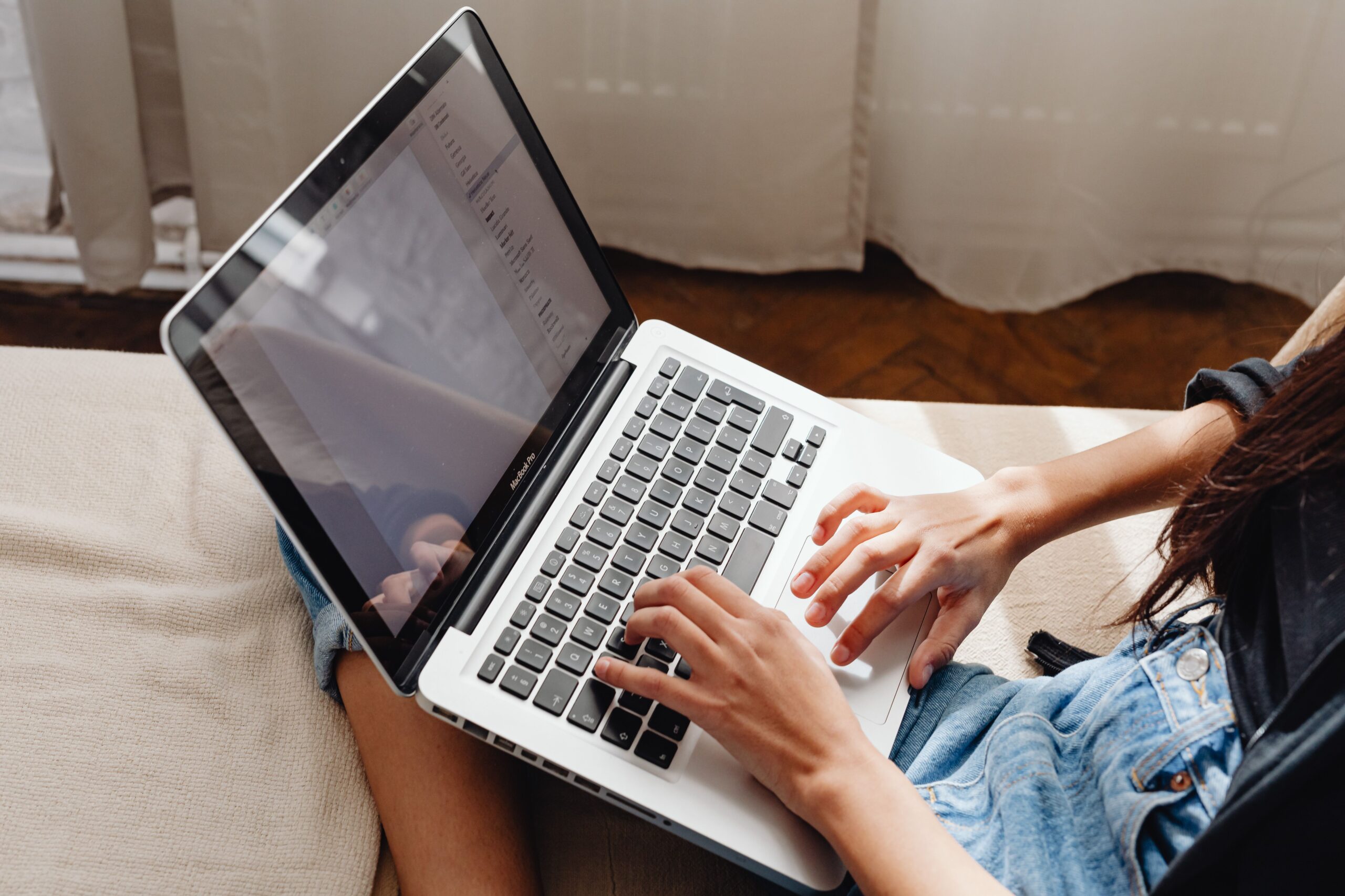 Close-up of a woman's hands typing on a laptop while sitting comfortably indoors.